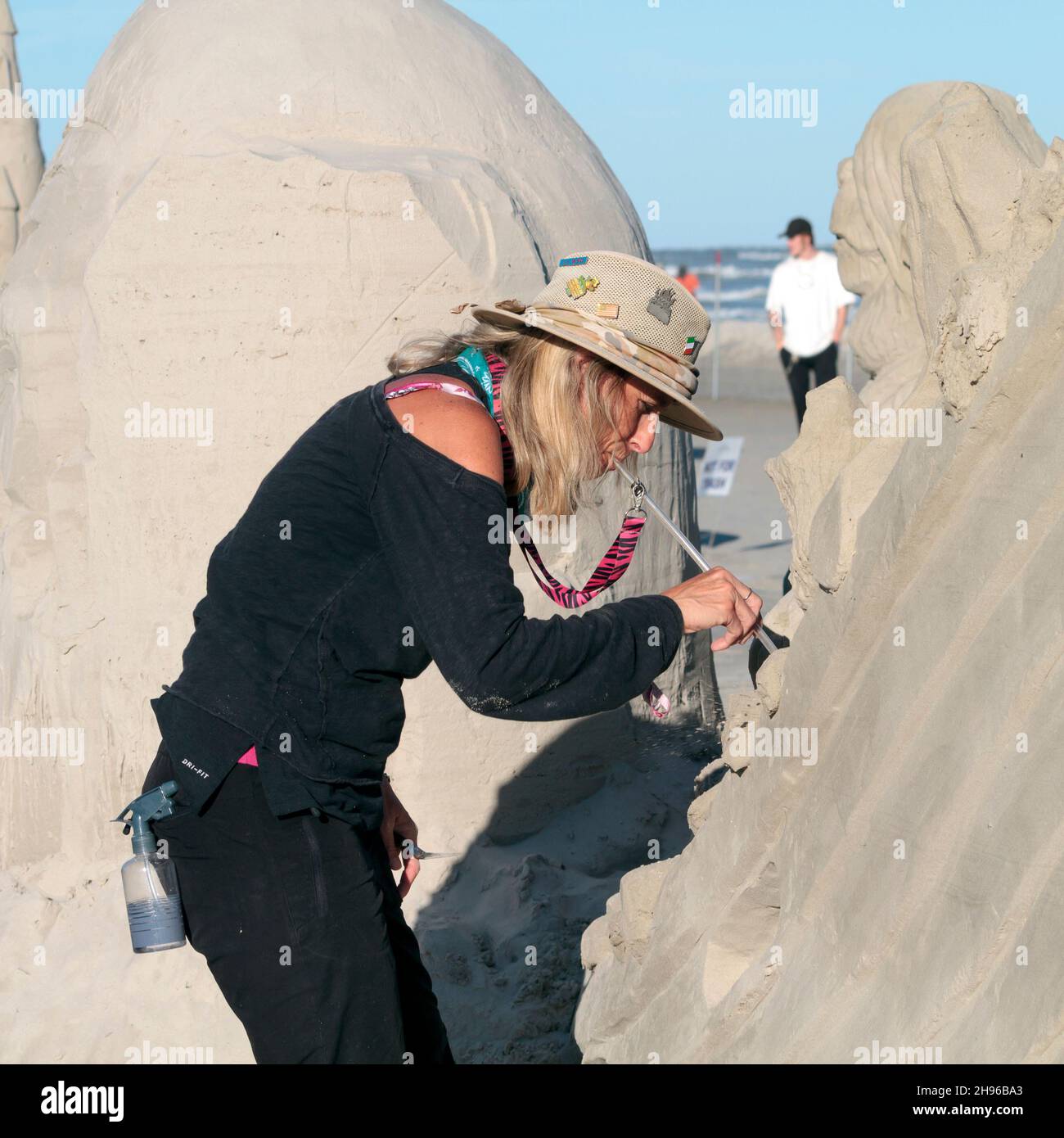 Laura Cimador-Gowdy stimmt ihre Sandskulptur mit einem Blasrohr beim Texas Sandfest 2021 in Port Aranlas, Texas, USA, fein. Stockfoto