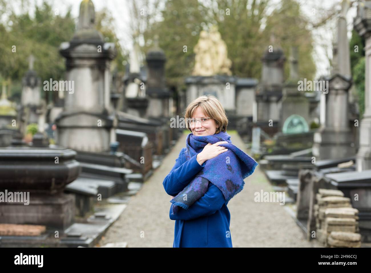 Porträt einer 30-jährigen Frau mit blauem Wintermantel und Schal auf einem Friedhof Stockfoto