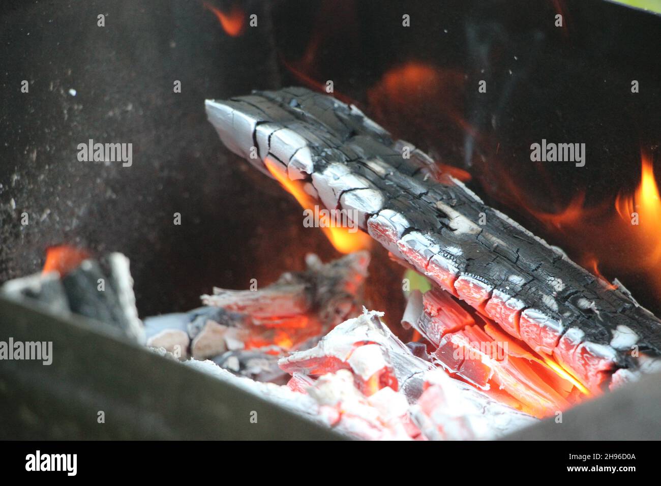 Schwelende Asche eines Lagerfeuers. Feuer brennt in der Nähe am Lagerfeuer. Stockfoto