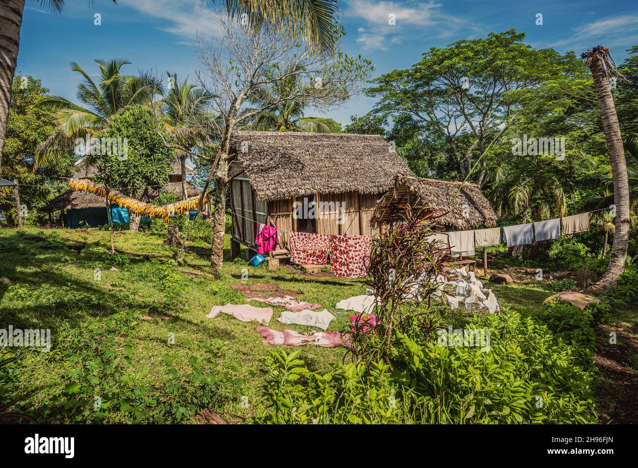 Die Wäsche trocknet auf Seilen in einem Hof aus alten Hütten, umgeben von tropischen Pflanzen unter dem Sonnenlicht Stockfoto