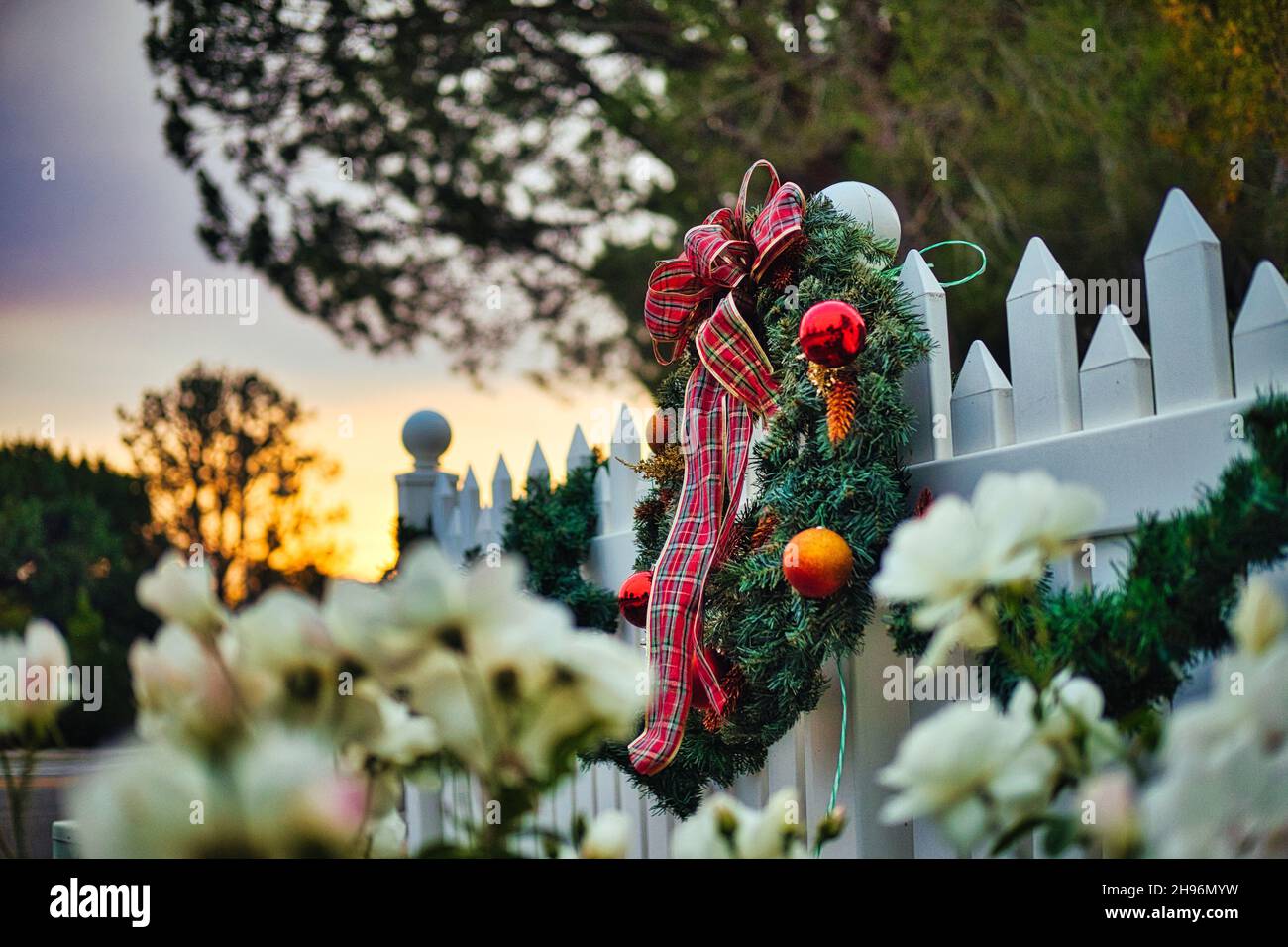Weihnachtskranz auf einem Pfostenzaun bei Sonnenuntergang mit Blumen Stockfoto