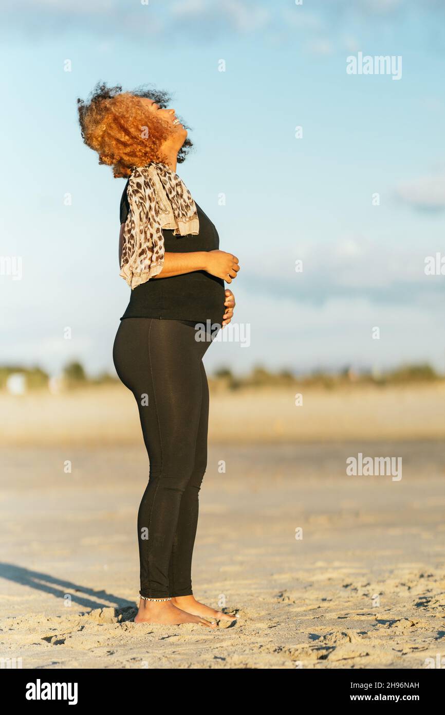 Profil einer Schwangeren Latina, die in Sportkleidung am Strand steht Stockfoto