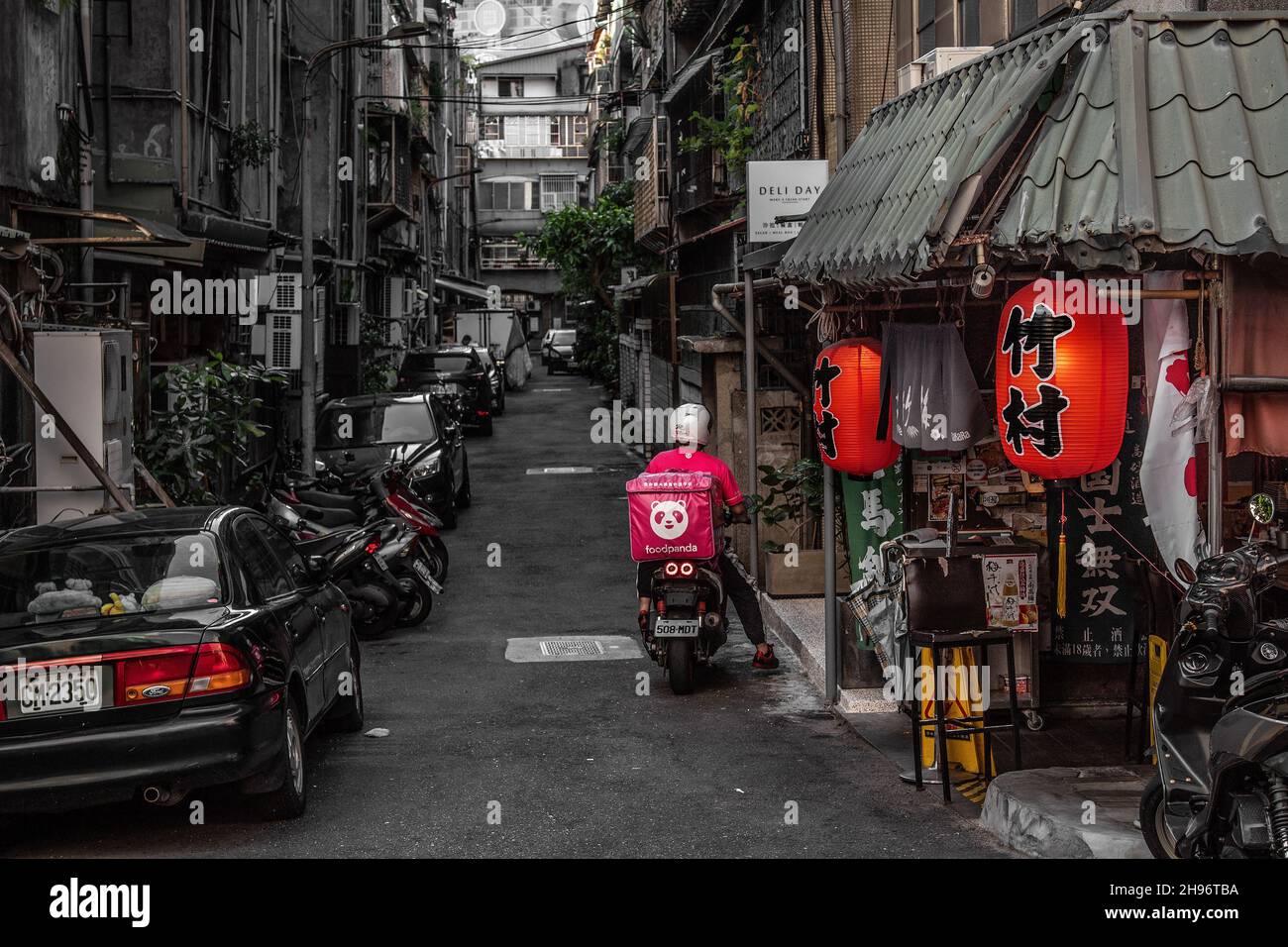 Ein einziger Lieferfahrer auf einem Moped, auf einer launischen städtischen Gasse/Straße vor einem Restaurant im Xinyi-Viertel von Taipei, der Hauptstadt Taiwans. Stockfoto
