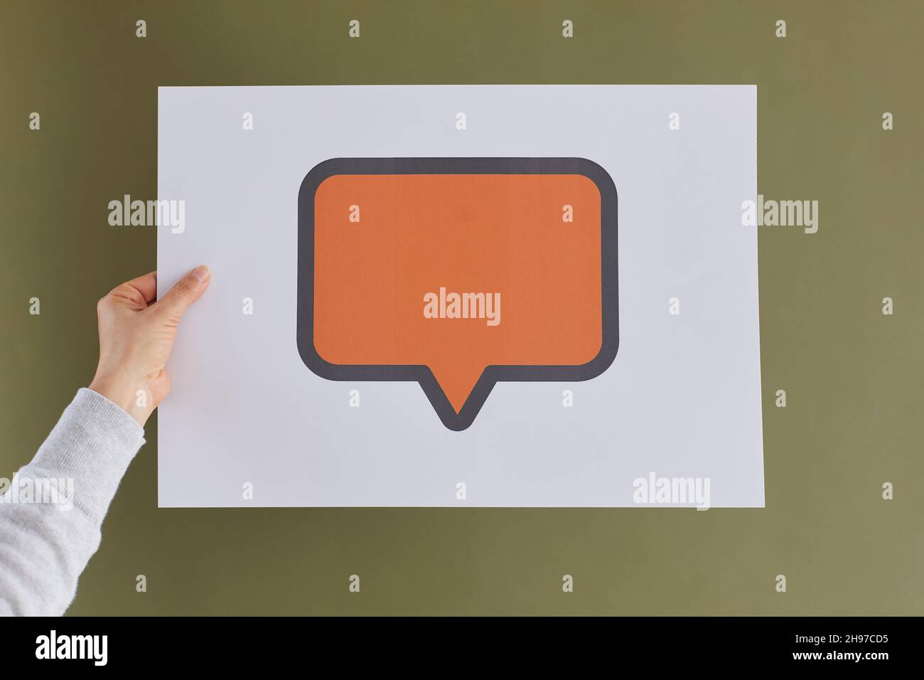 Menschliche Hand, die eine Karte mit einem orangefarbenen Sprechballon oder einer Nachrichtenblase hält Stockfoto
