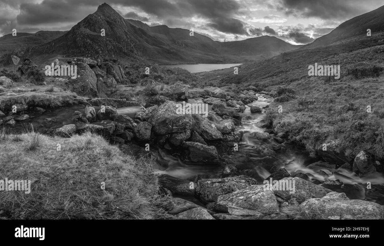 Schwarz-Weiß Episch dramatisch Herbstaufnahme der Sonnenuntergänge von Llyn Ogwen und Tryfan im Snowdonia Nationalpark mit Bach und Felsen im Vordergrund Stockfoto