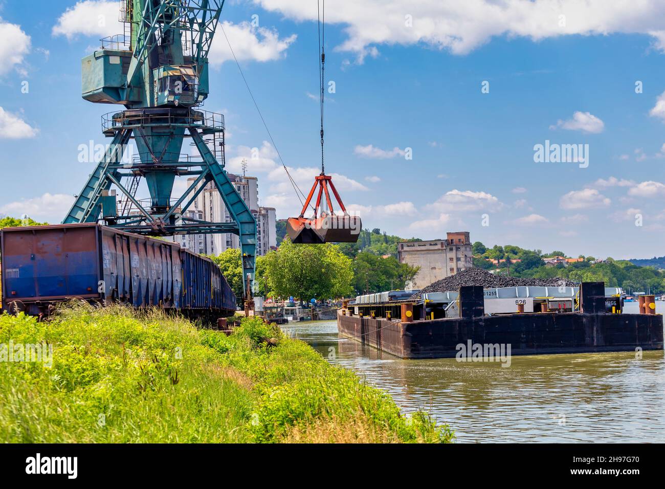 Kran entladen Kohle von Lastkahn zu Zug Wagen am Flusshafen. Stockfoto