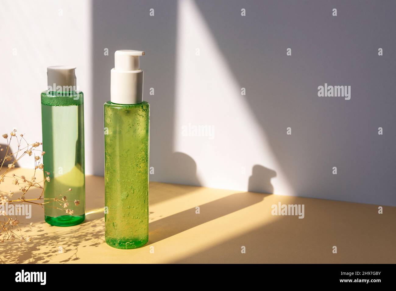 Grüne Kosmetikflaschen mit Gesichtswaschgel und Tonic auf beigem Tisch. Trockene Gypsophila Blumen Dekoration. Natürliche Bio-Kosmetik-Konzept. Modell Stockfoto