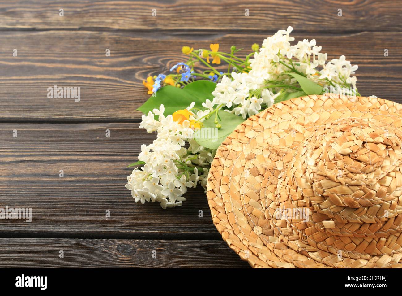 Blumenstrauß in einem Strohhut auf einem hölzernen Hintergrund Stockfoto