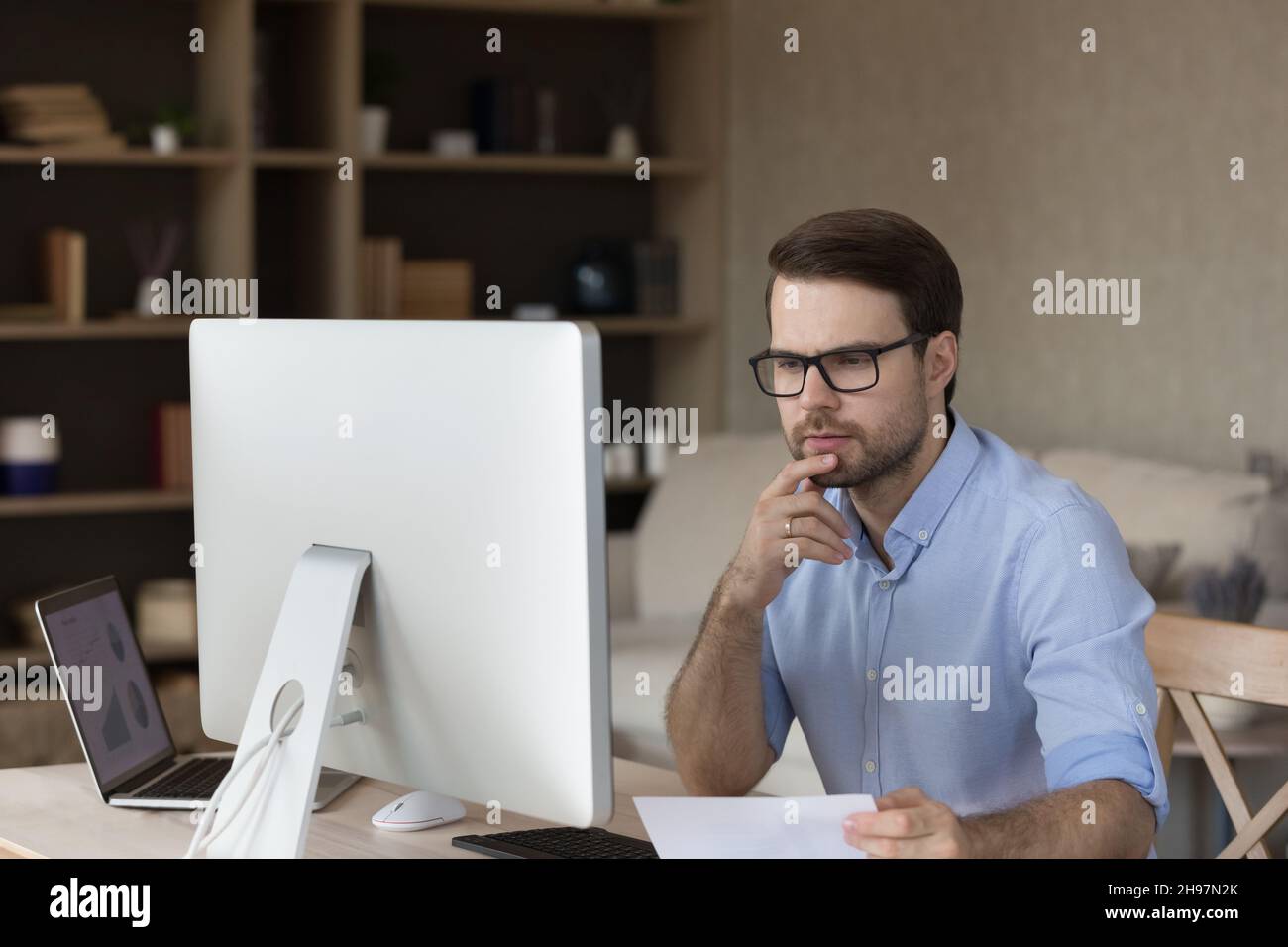 Fokussierter, tausendjähriger Geschäftsmann mit Brille, der über das Projekt am Arbeitsplatz nachdenkt Stockfoto