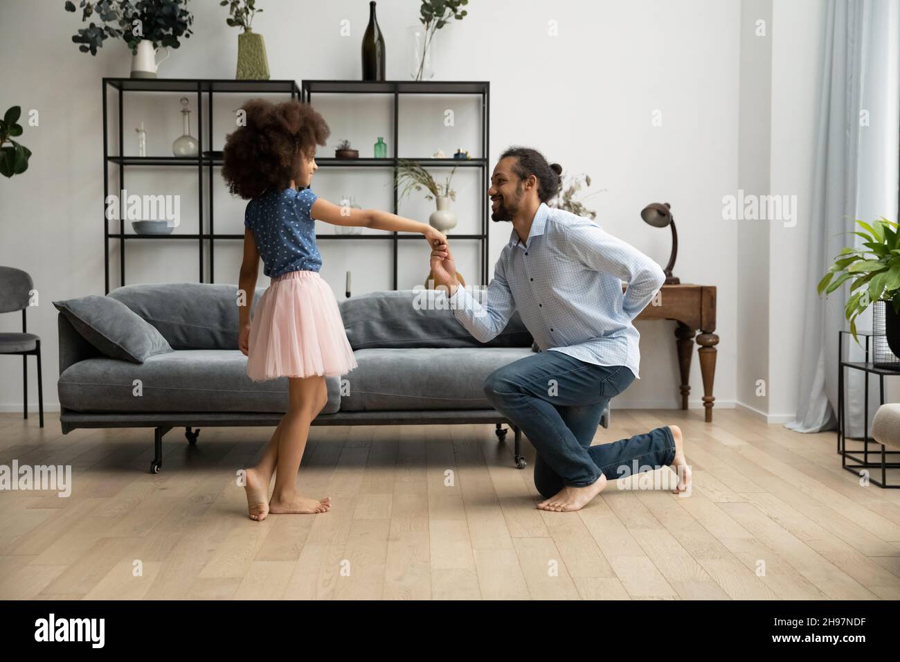 Glücklicher afroamerikanischer Vater lädt zum Tanz kleine Tochter Kind. Stockfoto