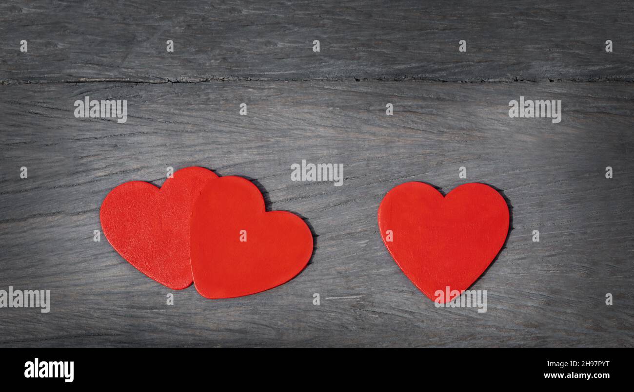 Drei Herzen auf einem hölzernen Hintergrund. Rote Herzen auf grauem altem Holz. Paare Herzen und ein Herz Stockfoto