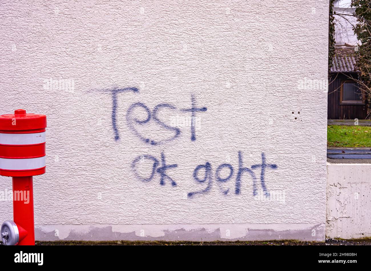 Hydrant vor einer weißen, mit Graffiti bedeckten Gebäudewand mit der deutschen Aufschrift „Test ok geht“. Stockfoto