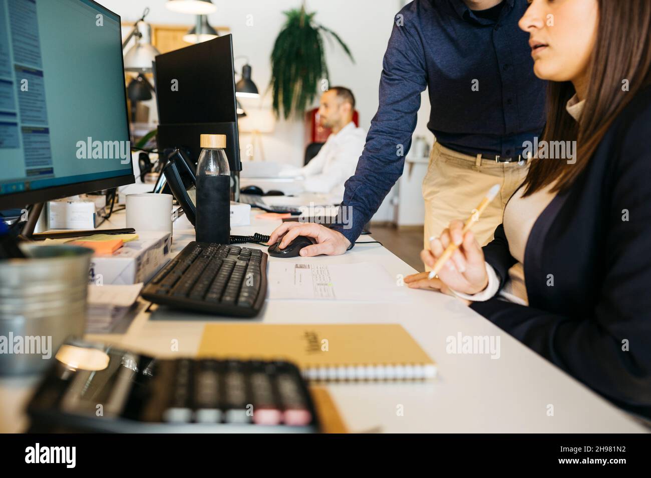 Nahaufnahme der Hände eines Mannes mit dem Computer seines Kollegen auf einem unordentlichen Schreibtisch im Büro. Arbeiten zusammen Stockfoto