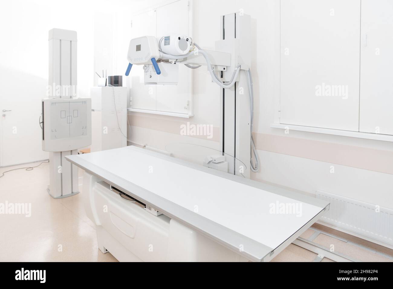 Röntgenabteilung im modernen Krankenhaus. Röntgenraum mit Scangerät und leerem Bett. Techniker, der ein Röntgengerät anpasst. Scannen von Brust, Herz Stockfoto