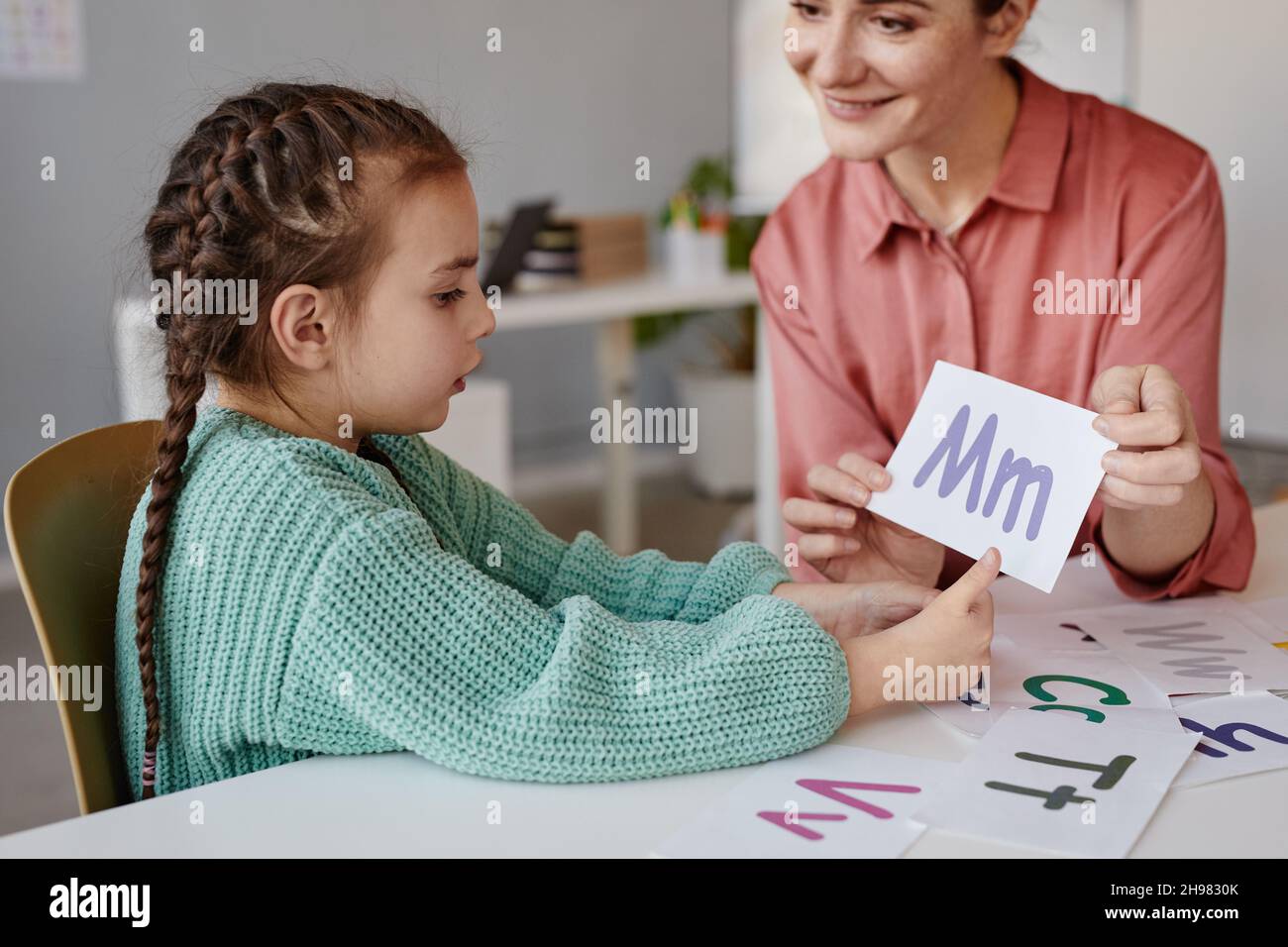 Kleines Mädchen, das zusammen mit dem Tutor am Tisch das englische Alphabet lernt Stockfoto