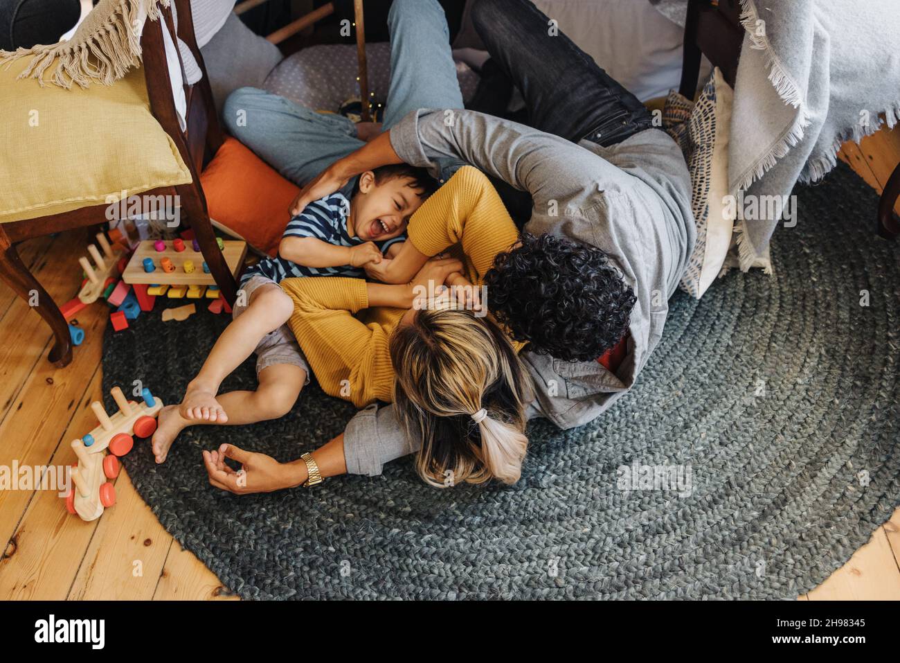 Draufsicht auf einen kleinen Jungen, der Spaß mit seiner Mutter und seinem Vater in ihrem Spielplatz hat. Junger Junge lacht fröhlich, während er mit seinen Eltern spielt. Familie der t Stockfoto