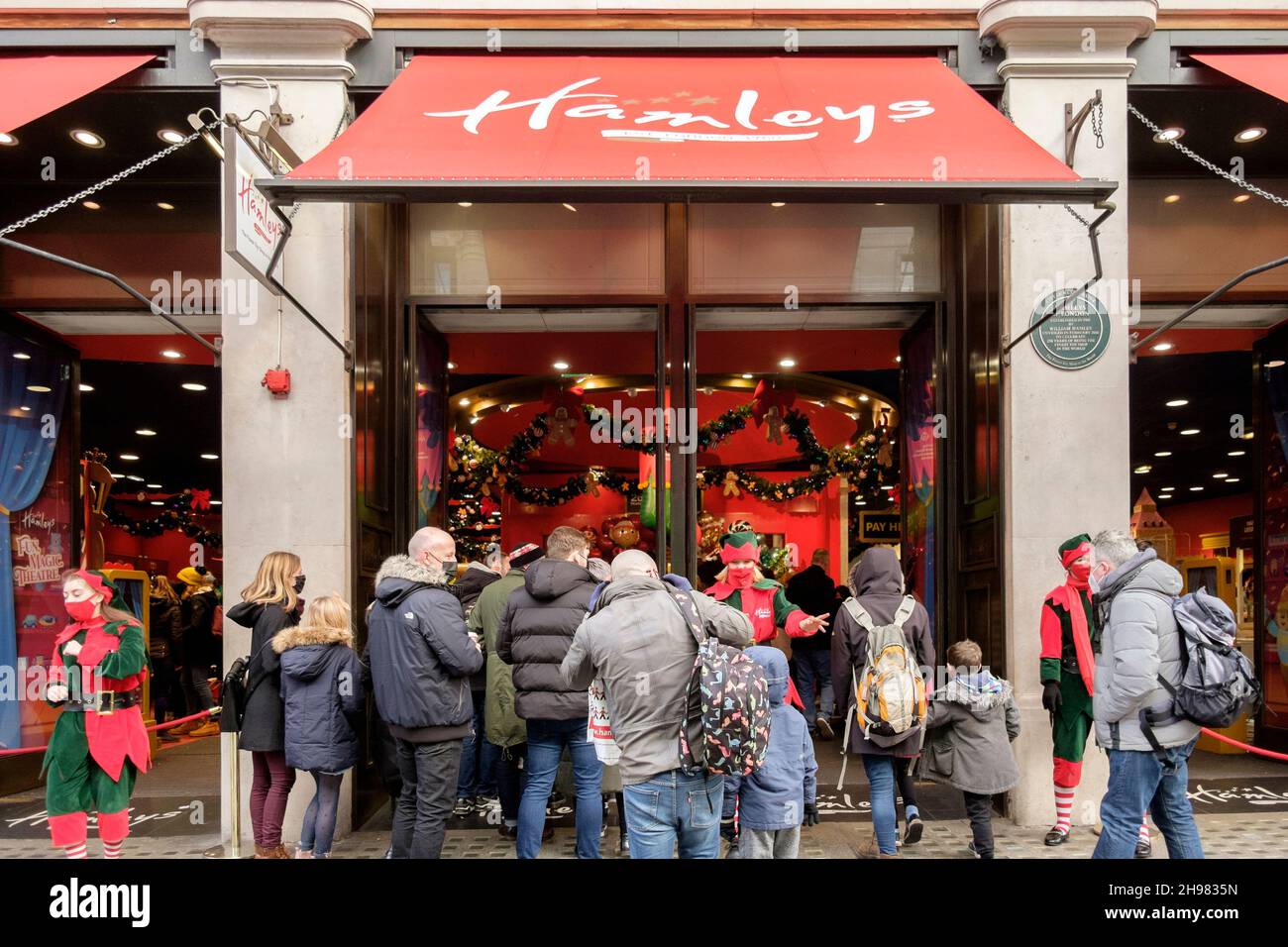 4th. Dezember 2021: Weihnachtseinkäufer im Hamleys-Spielzeugladen in der Regent Street werden von Arbeitern begrüßt, die als Elfen mit Gesichtsbezügen bekleidet sind. Die britische Regierung hat Maßnahmen neu erlassen, die es zu einer rechtlichen Verpflichtung machen, Gesichtsbezüge in Geschäften und öffentlichen Verkehrsmitteln zu tragen, sofern sie nicht vom 30th. November ausgenommen sind, weil sie Bedenken wegen der Omicron-Variante von covid-19 hatte. London, Großbritannien. Stockfoto