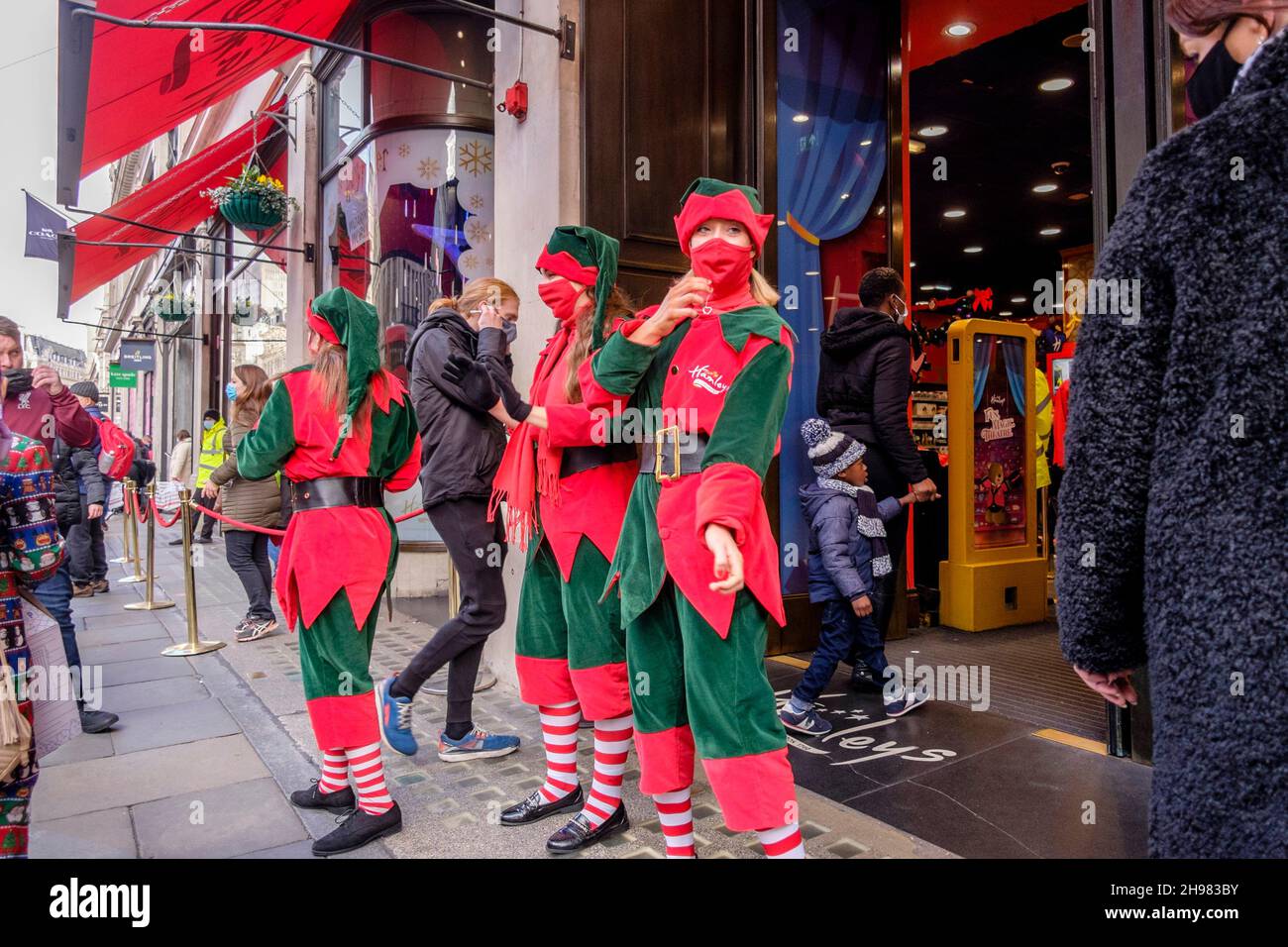 4th. Dezember 2021: Weihnachtseinkäufer im Hamleys-Spielzeugladen in der Regent Street werden von Arbeitern begrüßt, die als Elfen mit Gesichtsbezügen bekleidet sind. Die britische Regierung hat Maßnahmen neu erlassen, die es zu einer rechtlichen Verpflichtung machen, Gesichtsbezüge in Geschäften und im öffentlichen Verkehr zu tragen, sofern sie nicht vom 30th. November ausgenommen sind, weil sie Bedenken wegen der Omicron-Variante von Covid-19 hatte. London, Großbritannien. Stockfoto