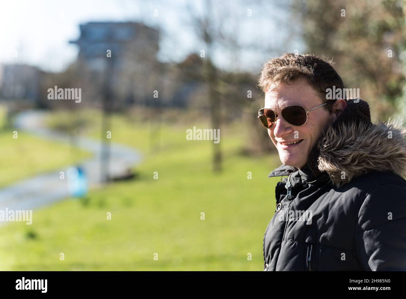 Außenportrait eines Mannes mit einem pelzigen Wintermantel, der eine Sonnenbrille in einem Brüsseler Park trägt Stockfoto
