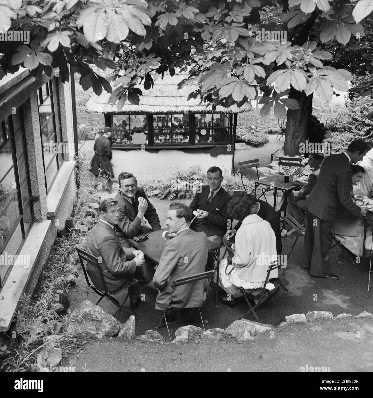 Cheddar, Sedgemoor, Somerset, 20/06/1953. Eine Gruppe von Menschen saß vor einem Café in Cheddar, während eines Laing-Personals, das nach Minehead ging. Im Jahr 1947, nach einer siebenjährigen Pause, hatte Laing seine „Ausflüge in die Umgebung“ für Mitarbeiter und ihre Familien wiederbelebt, wobei die Reisen im Mai und Juni stattfinden. Diese Reise war für ihre Mitarbeiter in der Südwestregion aus Bristol und Plymouth. Die Aufnahme scheint in Cheddar aufgenommen worden zu sein, da sie auch hier auf der Reise angehalten haben. Stockfoto