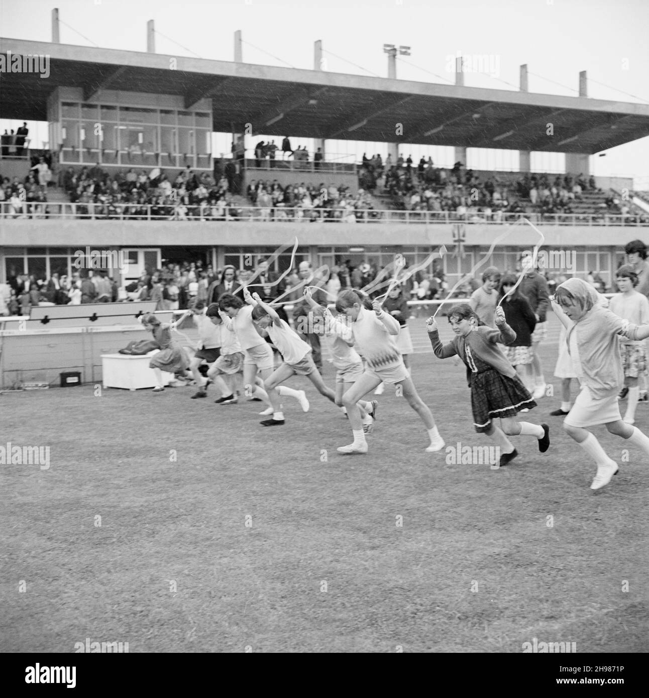 Copthall Stadium, Hendon, Barnett, London, 25/06/1966. Beim jährlichen Laing Sports Day im Copthall-Stadion verlassen die Mädchen die Startlinie eines Springsrennens mit Zuschauern in einem Stand darüber hinaus. Im Jahr 1966 fand am 25th. Juni der jährliche Laing Employees' Sports Day im Copthall Stadium in Hendon statt. Es war das erste Mal, dass die Veranstaltung dort stattfand, nachdem zuvor der Laing Sports Ground in Elstree stattgefunden hatte. Eine Reihe von Veranstaltungen umfasste Leichtathletik und einen Fußballwettbewerb, und die Teilnehmer reisten von den regionalen Büros und Standorten des Unternehmens, darunter aus Schottland und Carlisle. Es gab Stockfoto