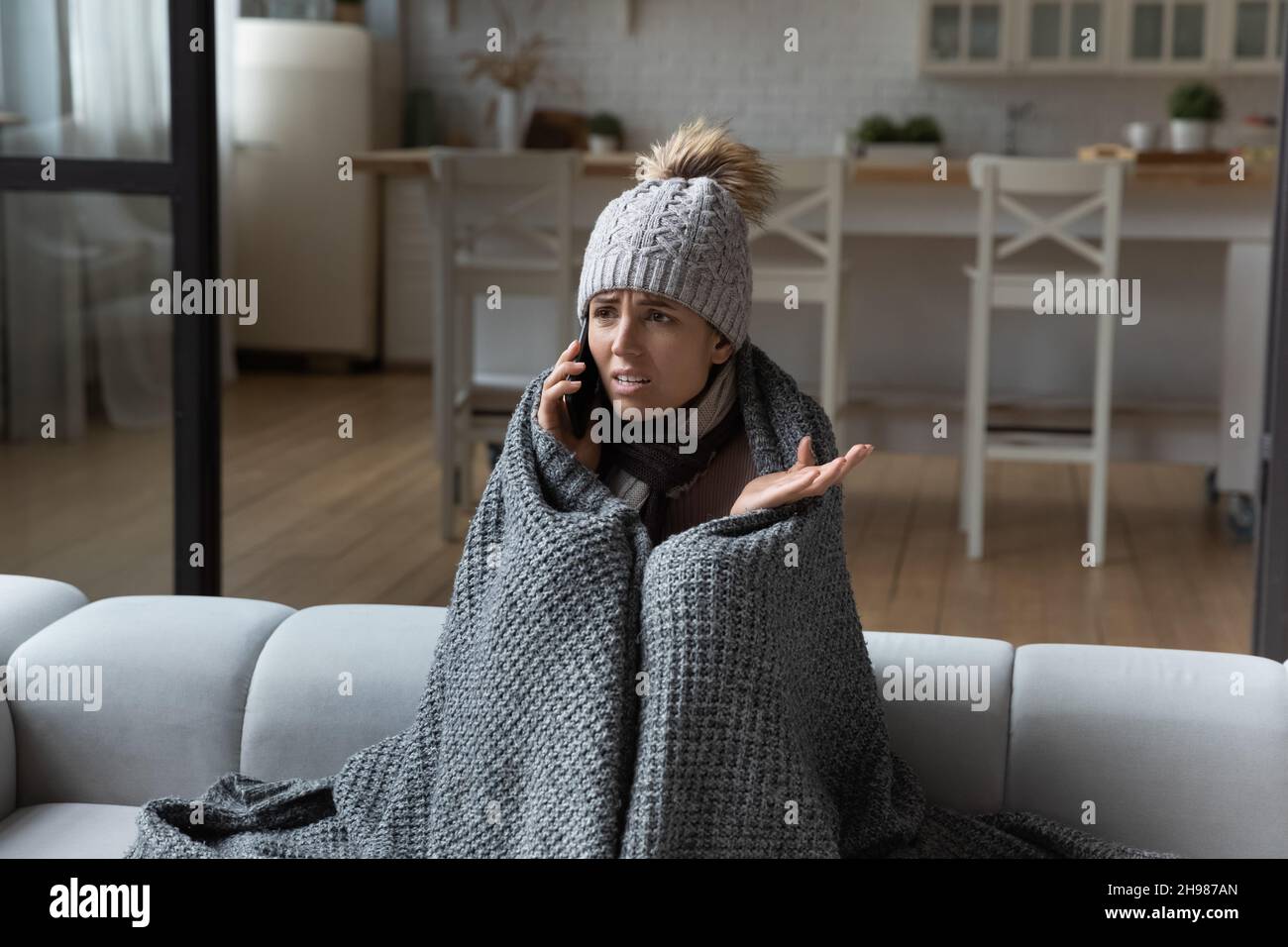 Frau in eine Decke gewickelt, die einen Telefonanruf macht, zu Hause kalt Stockfoto