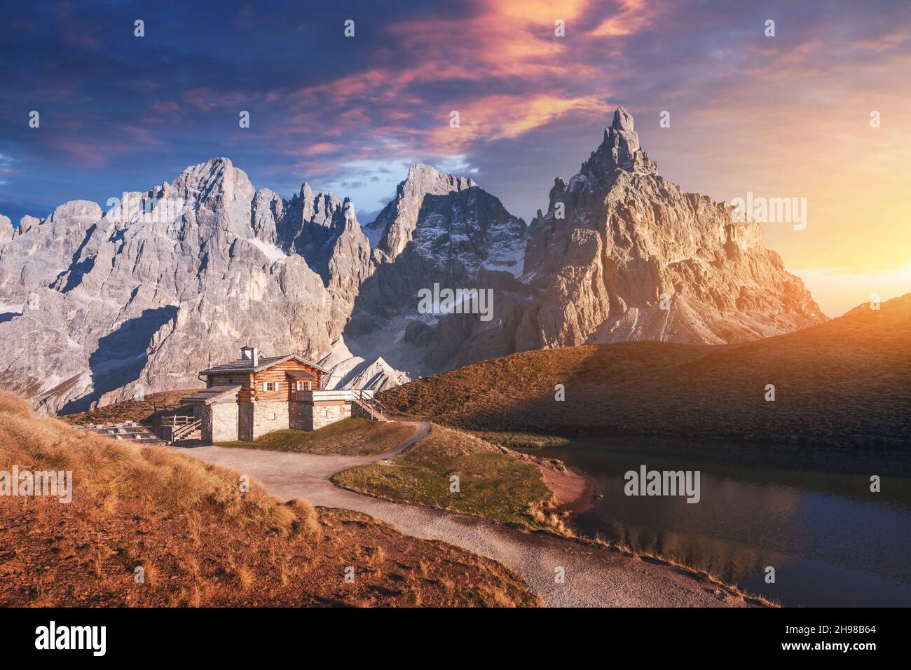 Unglaubliche Landschaft mit einer Reflexion des purpurnen Himmels und der Berge in einem Wasser des kleinen Sees in einem beliebten Touristenziel - Baita Segantini Berghütte. Rollepass, Dolomiten Alpen, Italien Stockfoto