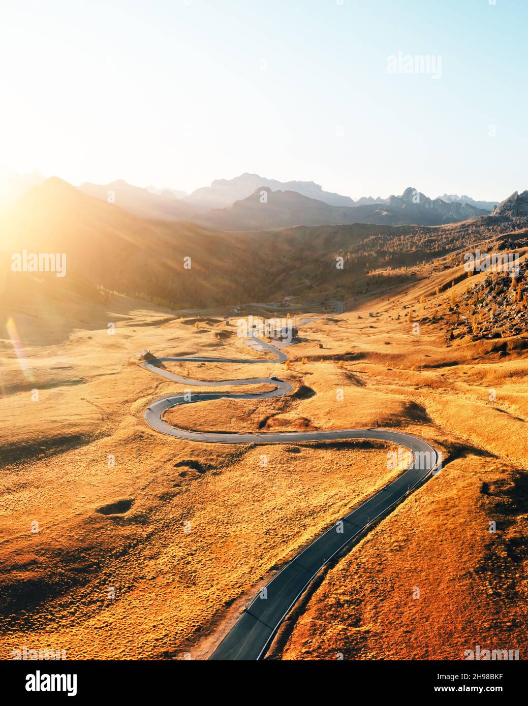 Malerische Luftaufnahme auf kurvenreicher Straße im herbstlichen Bergtal bei Sonnenuntergang. Das goldene Abendlicht beleuchtet die Berge und das orangefarbene Gras. Giau-Pass, Dolomiten, Dolomiten, Italien Stockfoto