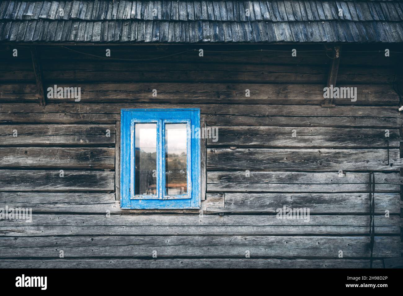 Holzhauswand mit Holzdach und blauem Cyan-Fenster auf altes ukrainisches Haus Stockfoto