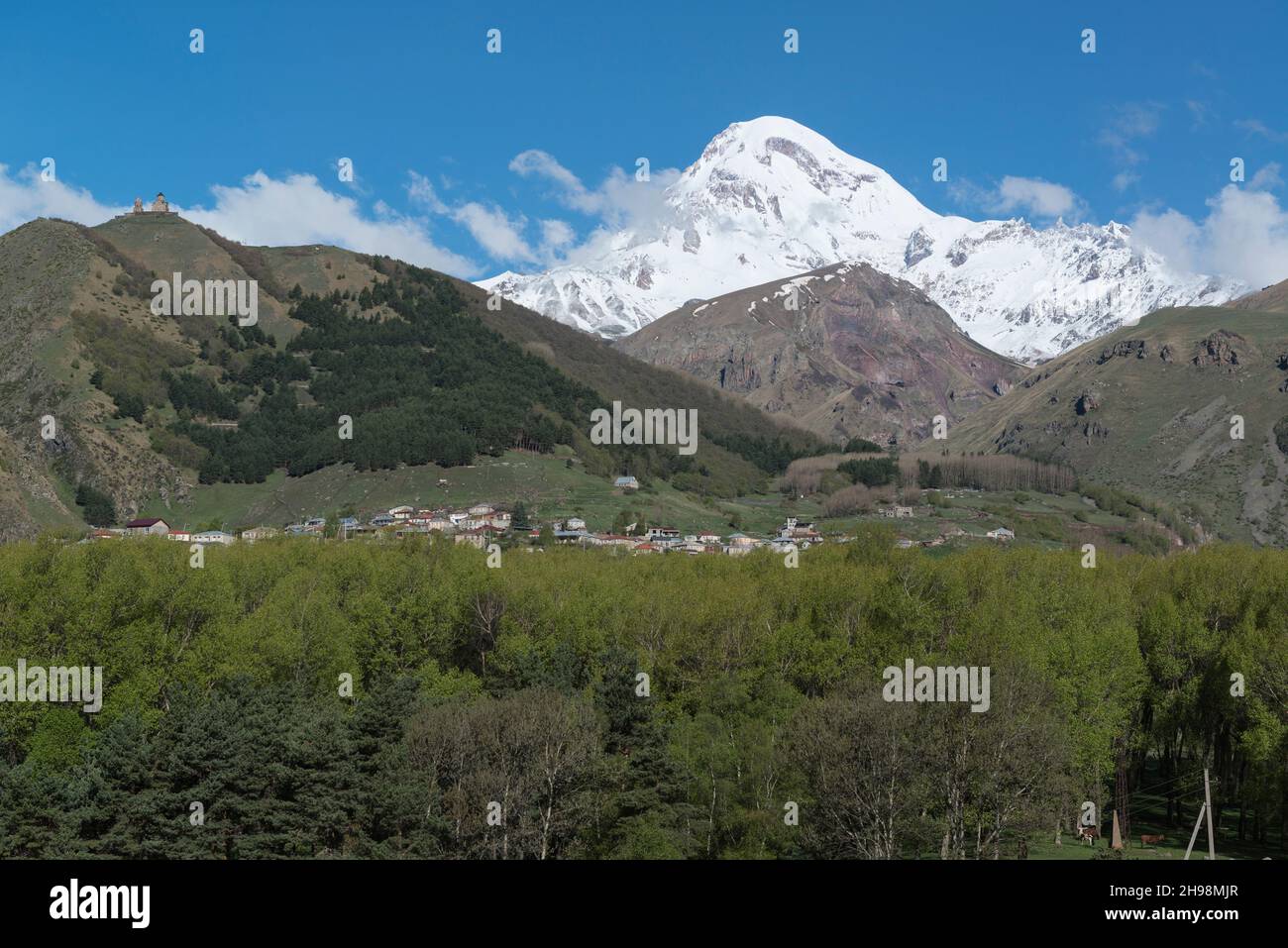 Auf dem Hügel auf der linken Seite befinden sich die dominante schneebedeckte Kirche des Kazbek-Berges und der Gergeti-Dreifaltigkeitskirche. Stepantsminda, Mzcheta-Mtianeti-Region, Georgien, Kaukasus Stockfoto