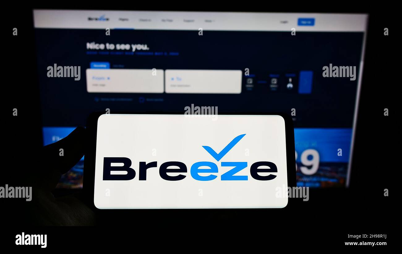 Person, die das Smartphone mit dem Logo der US-amerikanischen Fluggesellschaft Breeze Airways auf dem Bildschirm vor der Website hält. Konzentrieren Sie sich auf die Telefonanzeige. Stockfoto