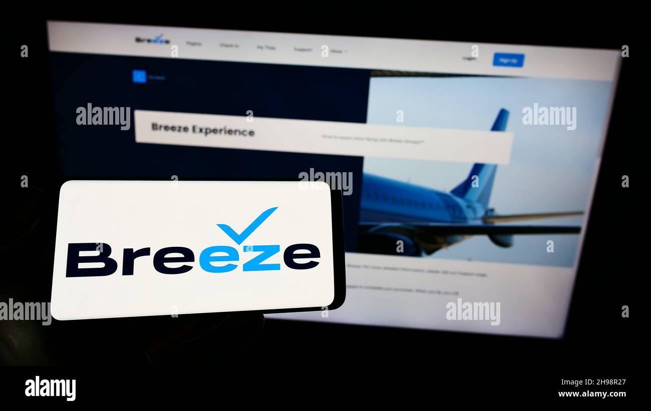 Person mit Mobiltelefon und Logo der amerikanischen Fluggesellschaft Breeze Aviation Group Inc. Auf dem Bildschirm vor der Webseite. Konzentrieren Sie sich auf die Telefonanzeige. Stockfoto