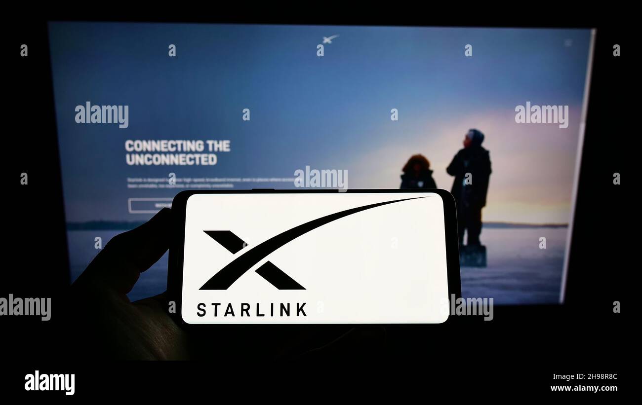 Person, die Mobiltelefon mit dem Logo der amerikanischen Satelliten-Internet-Firma Starlink (SpaceX) auf dem Bildschirm vor der Webseite hält. Konzentrieren Sie sich auf die Telefonanzeige. Stockfoto