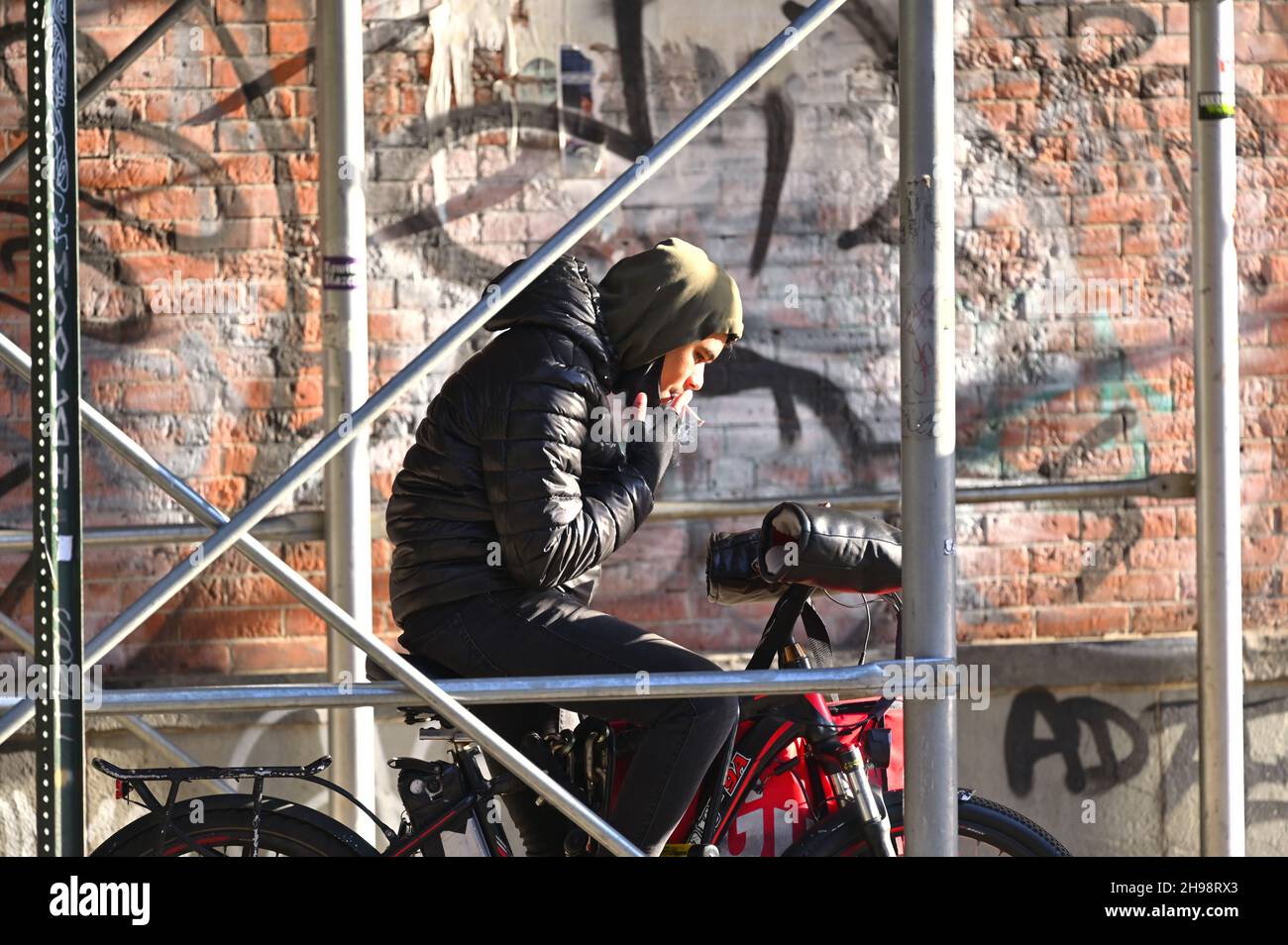 Ein junger Radfahrer studiert sein Telefon, während er in der Nähe einer mit Graffiti bedeckten Wand in Manhattan, New York City, NY, USA, raucht Stockfoto