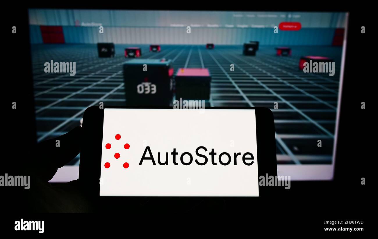 Person, die Mobiltelefon mit dem Logo des norwegischen automatisierten Speicherunternehmens AutoStore AUF dem Bildschirm vor der Webseite hält. Konzentrieren Sie sich auf die Telefonanzeige. Stockfoto