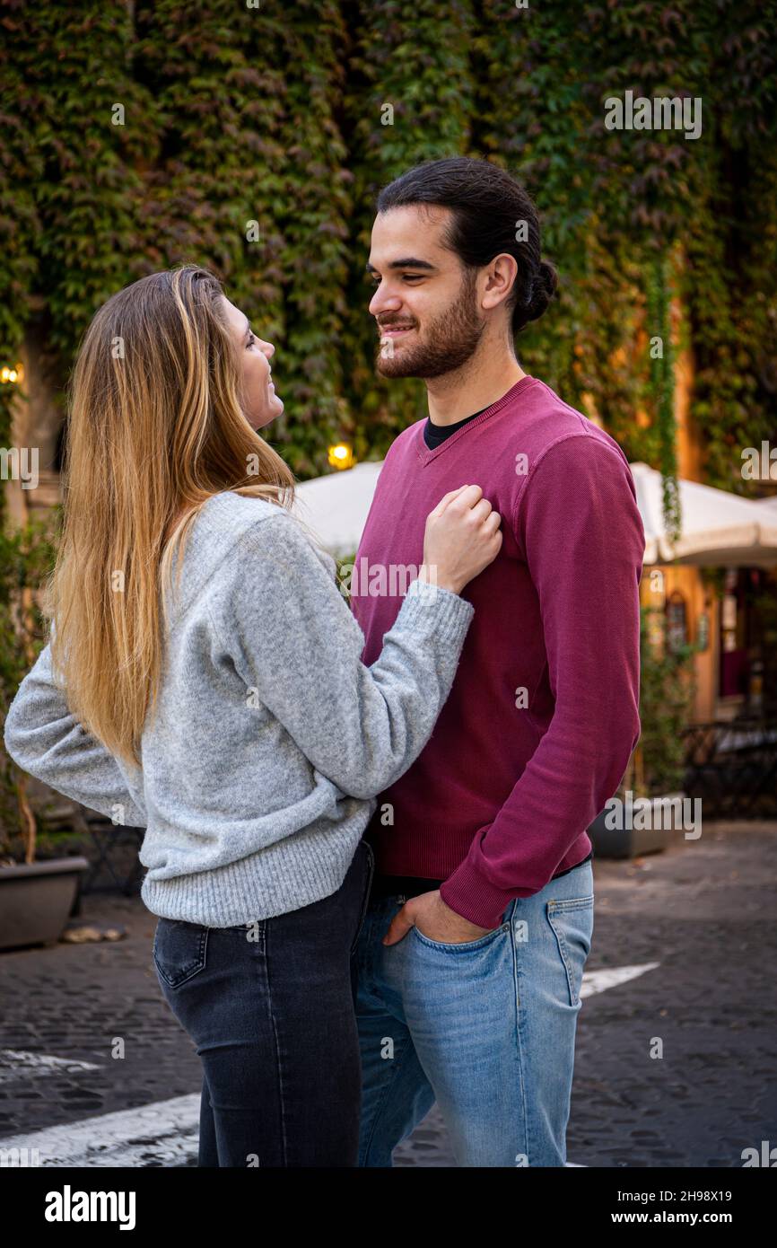 Junges Paar, das nach Rom reist. Die schöne blonde Frau umarmt ihren Freund und schaut ihr in die Augen. Im Hintergrund eine Straße im historischen Cent Stockfoto