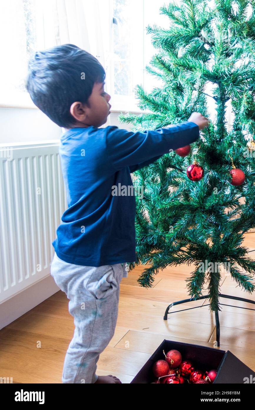Indischer Junge im Alter von 3 Jahren, der Weihnachtsbaum mit Kugeln schmückt Stockfoto