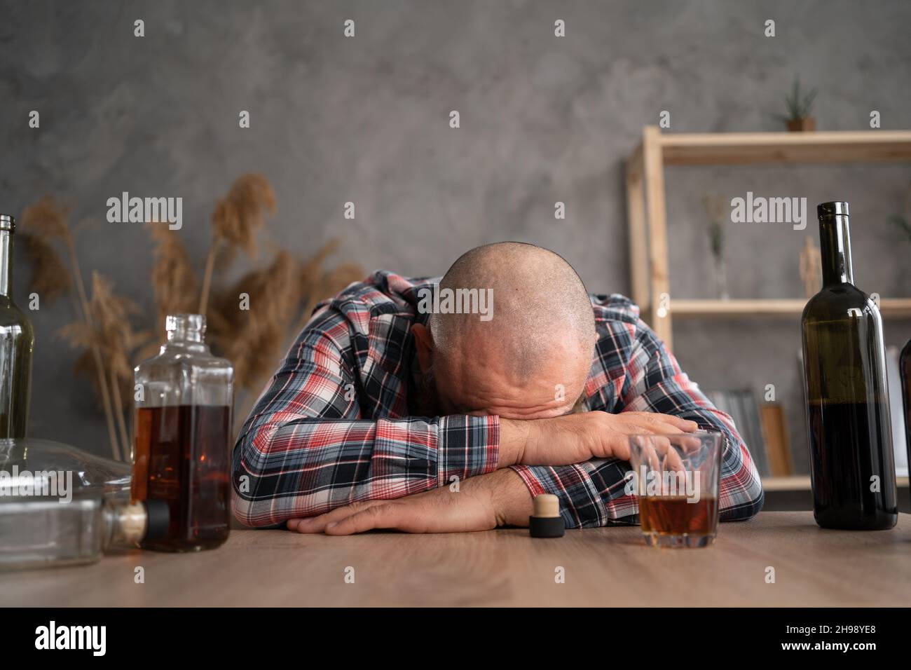 Alkoholismus, Alkoholabhängigkeit und Menschenkonzept - Alkoholiker liegen oder schlafen tagsüber auf dem Tisch unter leeren Alkoholflaschen. Stockfoto