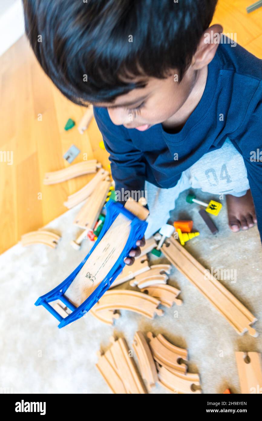 Junge spielt mit Zug Spielzeug. Indischer Junge im Alter von 3 Jahren, der mit einer hölzernen Eisenbahnstrecke und einem Zugsatz spielt Stockfoto