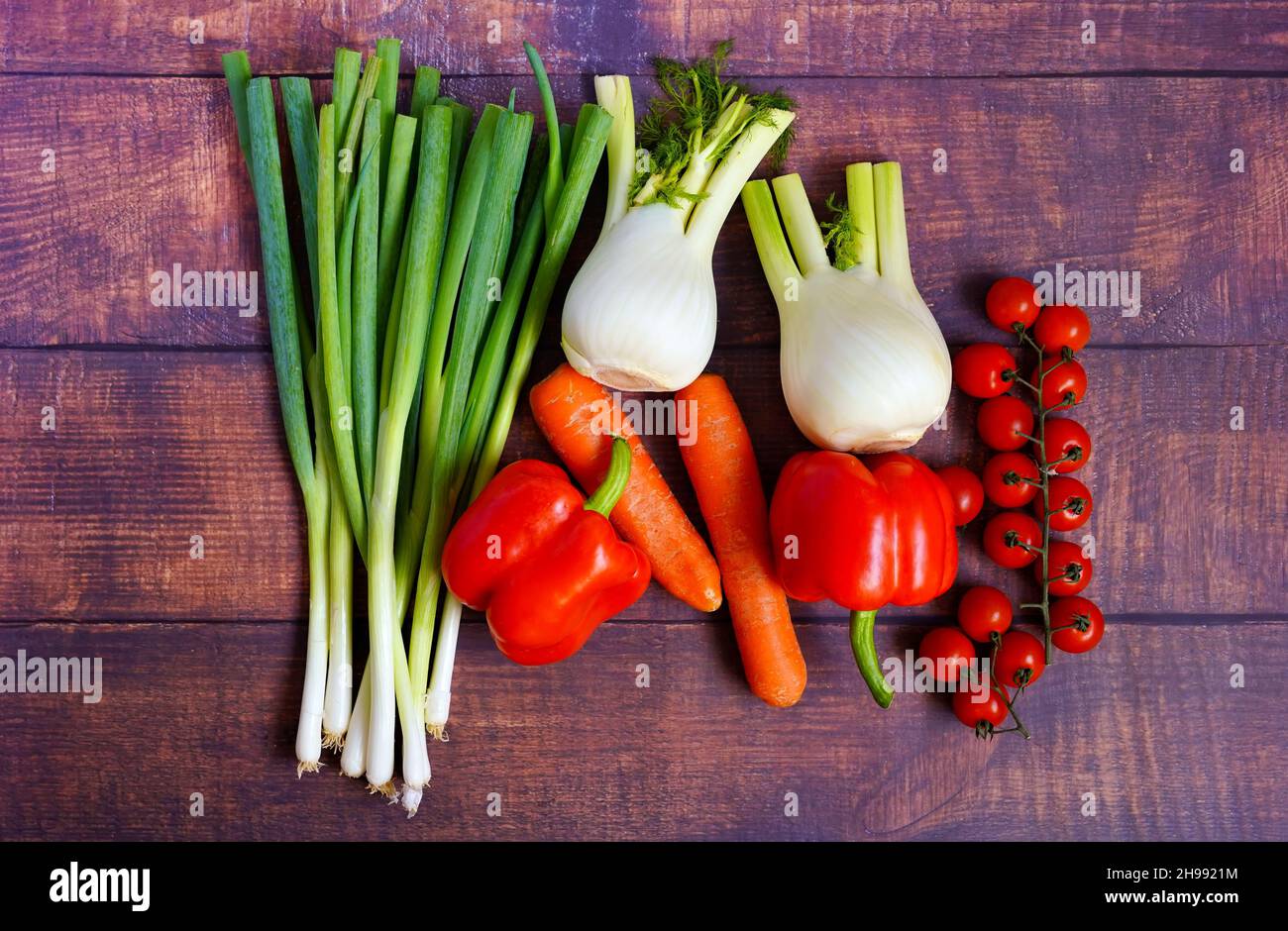 Frische Frühlingszwiebeln, Fenchel, Karotten, Tomaten und Paprika auf einem rustikalen Holztisch. Gesunde Zutaten für die Hausmannskost zur Unterstützung des Immunsystems. Stockfoto