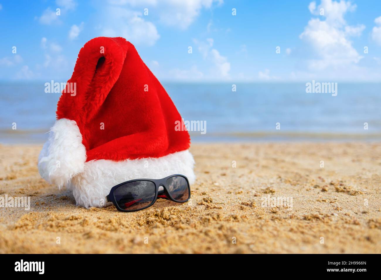 weihnachtsmütze und männliche Sonnenbrille am Sandstrand des Meeres. Stockfoto