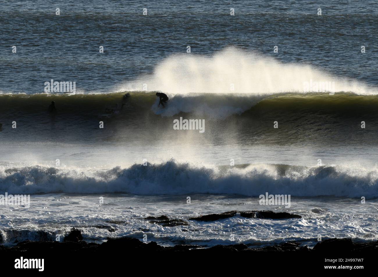 Surfen in Wales. Ein Surfer, der gegen die brechende hohle Wand der wve auf Crab Island geschildet wurde - ein starker Wind vor der Küste hebt das Spray in einer Wolke Stockfoto