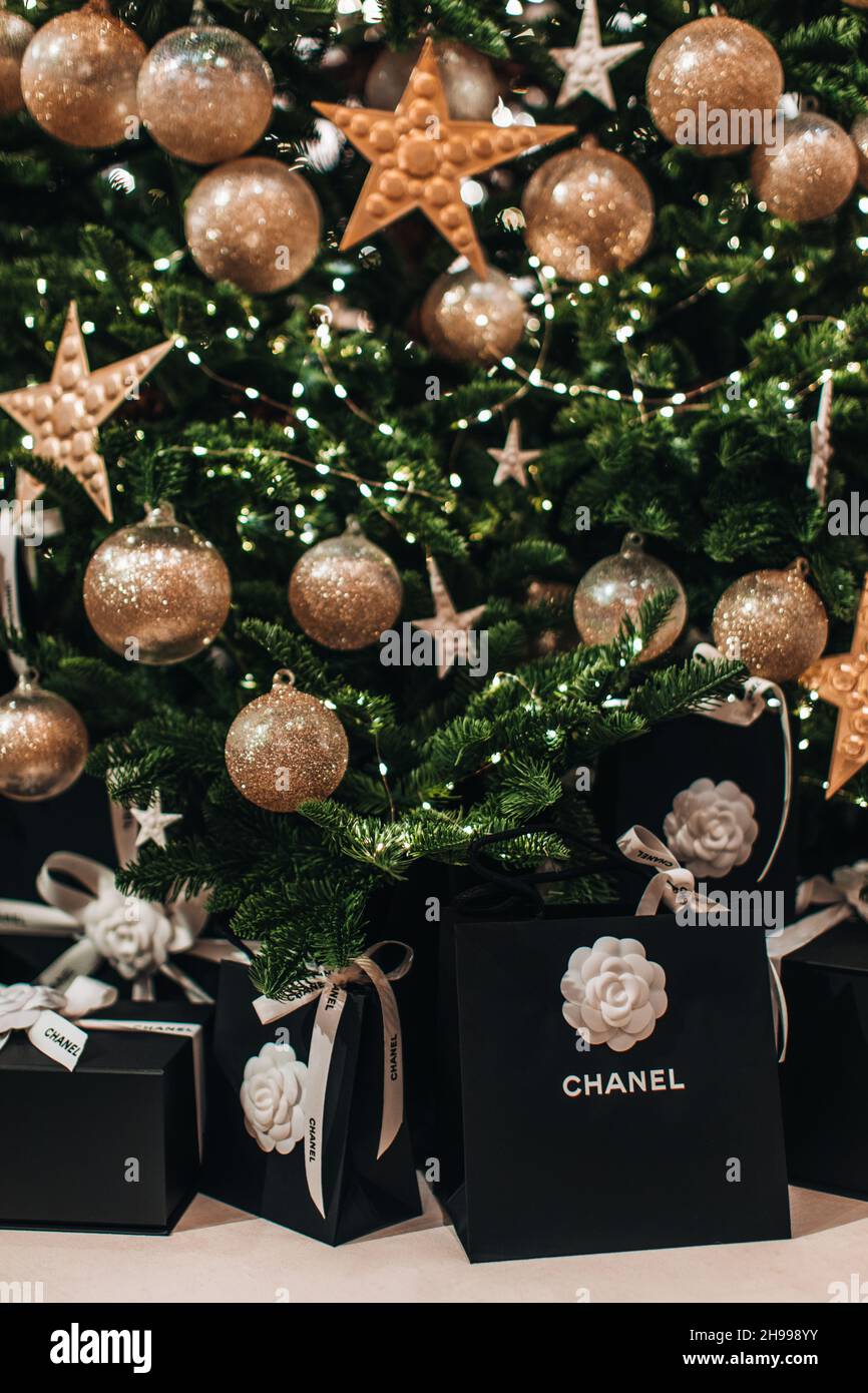 Weihnachtsgeschenk schwarze Tasche Chanel mit weißen seidigen Bändern unter dem Weihnachtsbaum mit goldenen Weihnachtskugeln. Neujahrs-Luxusgeschenke Stockfoto