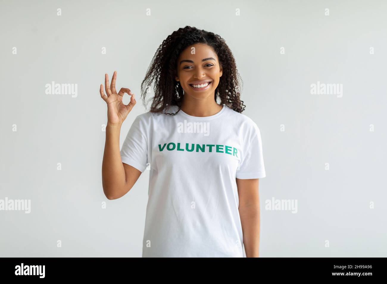 Freiwilligenarbeit während einer Pandemie. Glückliche afroamerikanische Freiwillige mit OK-Schild, die über der weißen Wand steht Stockfoto