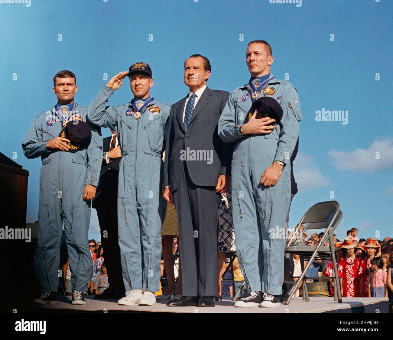 Präsident Richard M. Nixon und die Apollo 13-Besatzungsmitglieder ehren die Flagge der Vereinigten Staaten während der Zeremonien nach der Mission auf dem Luftwaffenstützpunkt Hickam, Hawaii. Die Astronauten James A. Lovell Jr. (Kapitän der US-Marine, begrüßt die Flagge), John L. Swigert Jr., Kommandomodulpilot (rechts) und Fred W. Haise Jr., Mondmodulpilot (links), wurden vom Chief Executive mit der Presidential Medal of Freedom ausgezeichnet. Der Apollo 13-Spritzwasserfall fand am 17. April 1970 um 12:07:44 Uhr (CST) statt, etwa eineinhalb Tage vor der Preisverleihung. Stockfoto