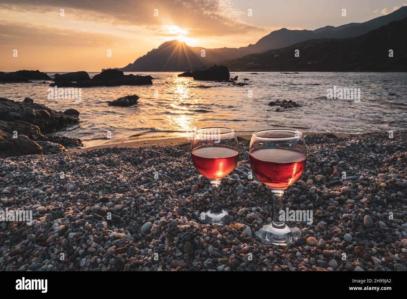 Genießen Sie ein Glas Rosenwein am Strand bei Sonnenuntergang Stockfoto