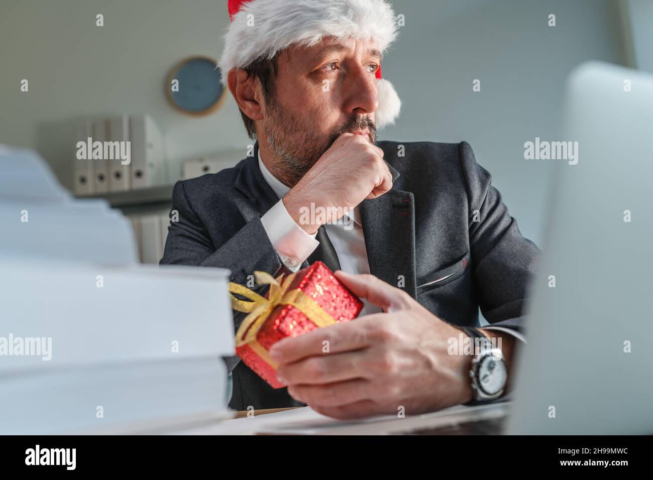 Besorgter Geschäftsmann mit Weihnachtsmannhut, der während der Weihnachtsfeiertage aus dem Bürofenster schaut, selektiver Fokus Stockfoto