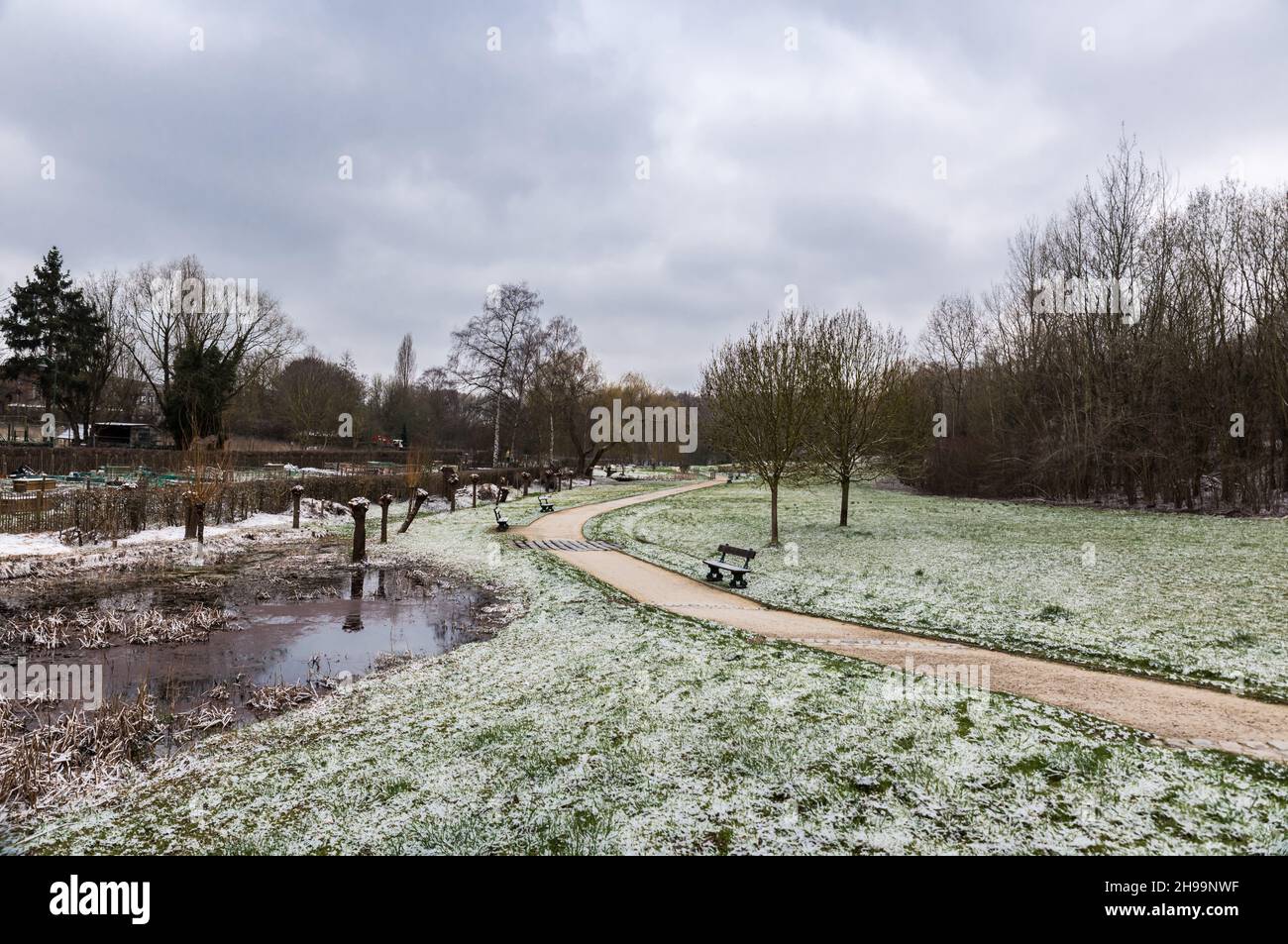Einsamer Stadtpark, der an einem frühen Wintermorgen mit frischer Schneeschicht bedeckt ist Stockfoto
