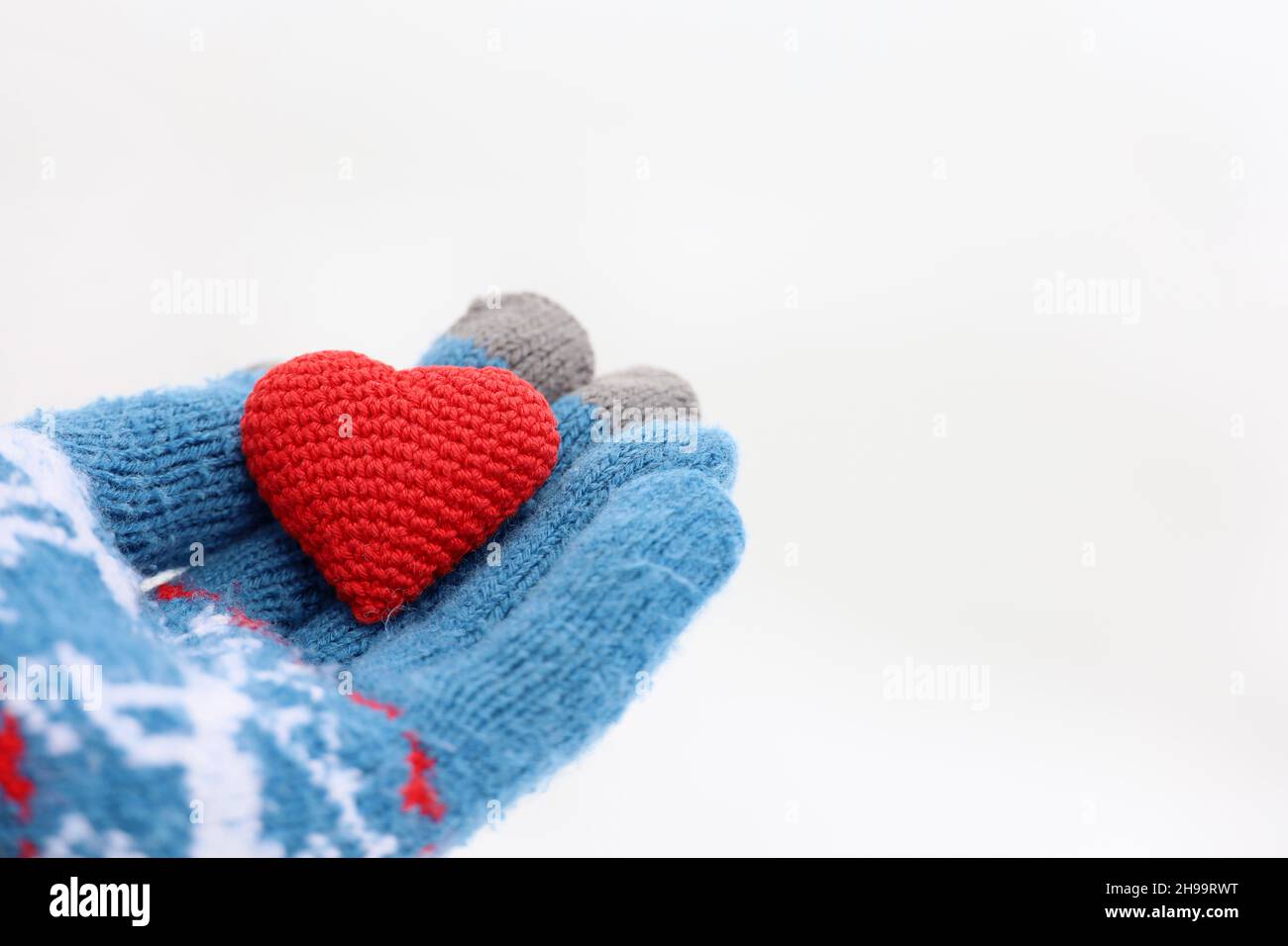 Rotes Herz auf Handfläche in warmem Strickhandschuh gegen den weißen Schnee. Konzept einer romantischen Liebe, Valentinstag oder Nächstenliebe Stockfoto