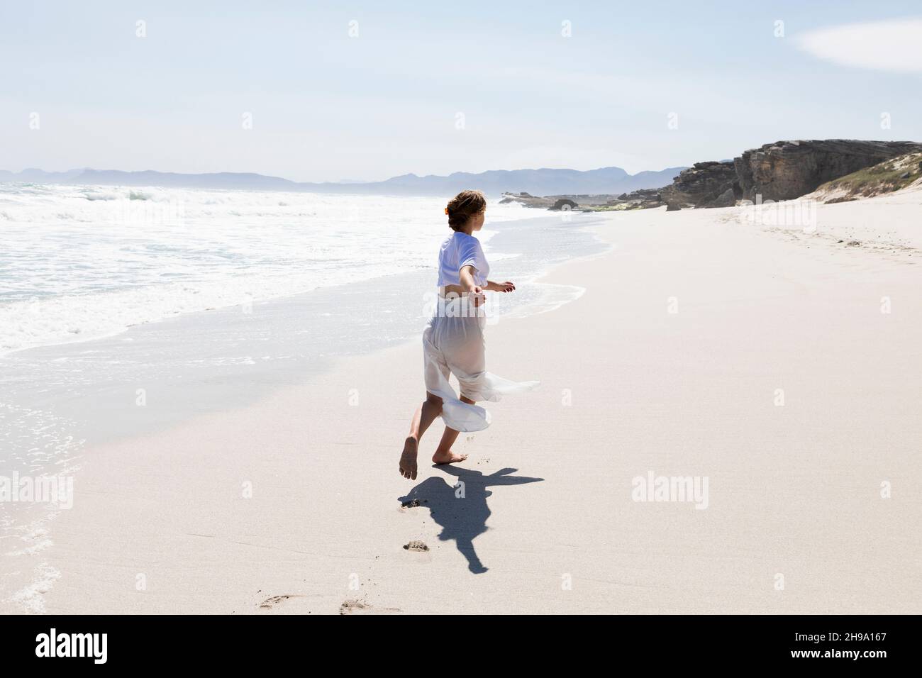 Teenager, die alleine an einem Sandstrand in Südafrika am Wasser tanzen Stockfoto